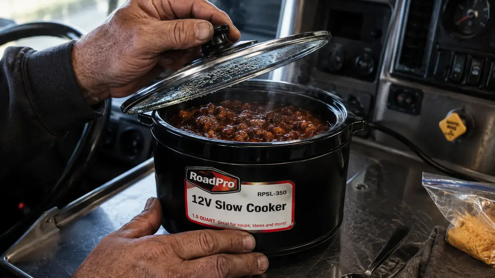 Hand lifting the lid off the RoadPro RPSL-350 slow cooker to reveal chili inside, steam rising