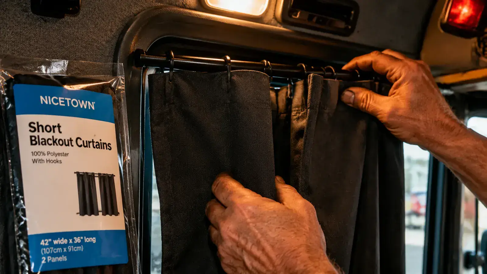 Hands hanging dark blackout curtain panels inside a semi truck sleeper bunk window