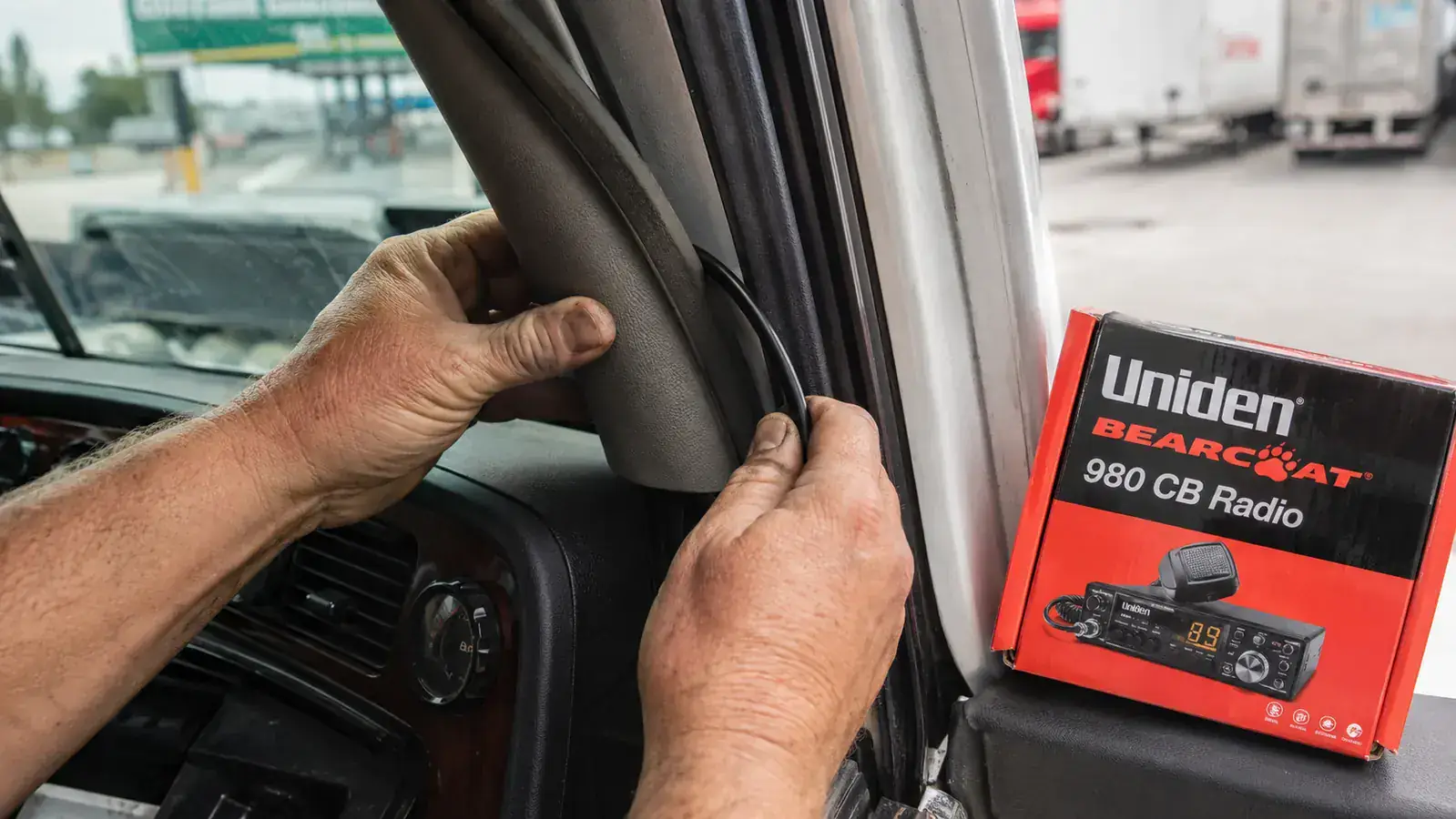 Hands routing a PL-259 coaxial cable along the A-pillar trim of a semi truck cab