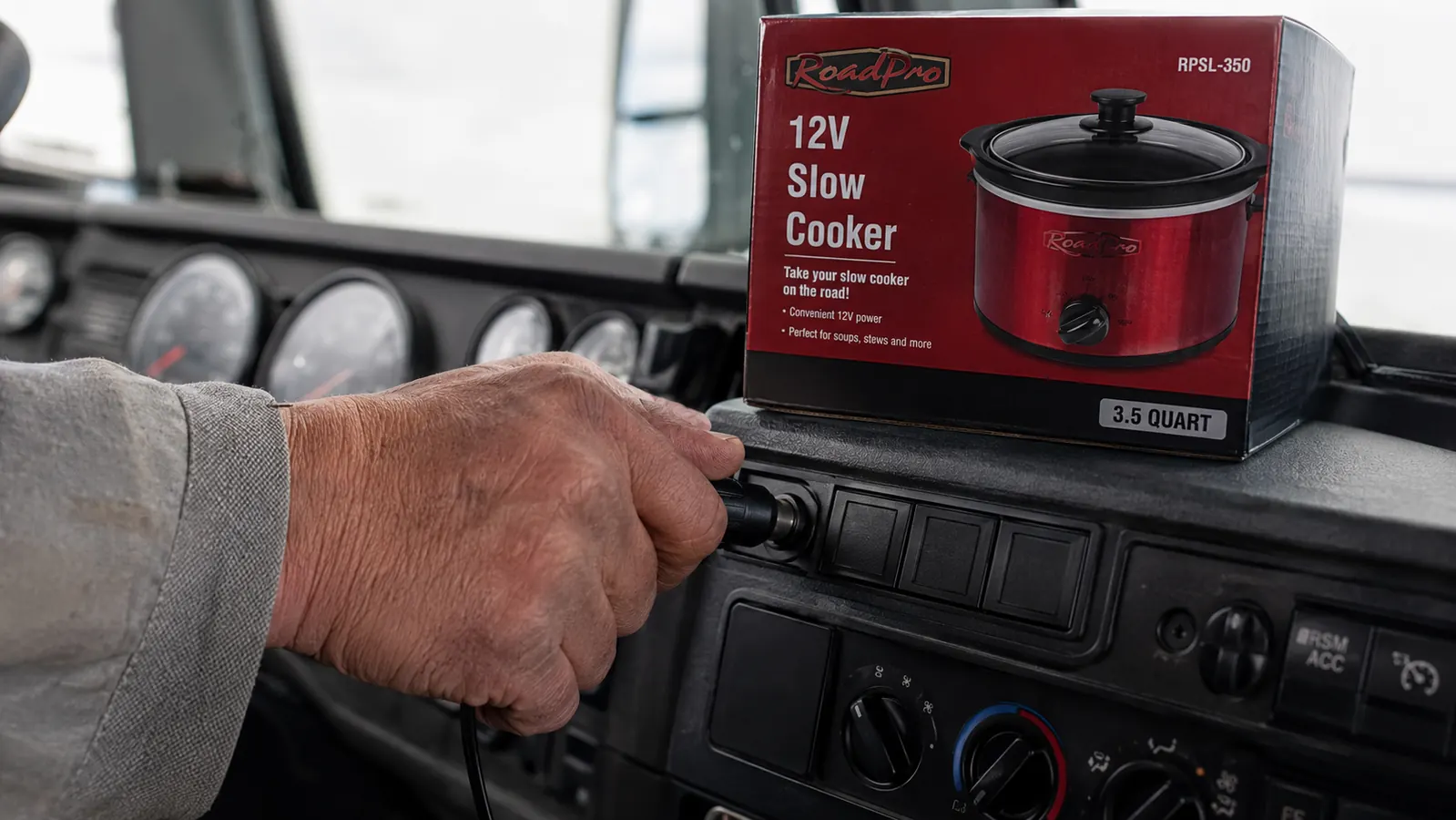 Hand plugging RoadPro slow cooker 12V cord into cigarette lighter outlet in a truck cab
